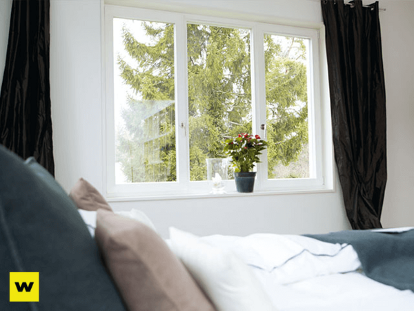 Helles Schlafzimmer mit gemütlichem Bett, großem Fenster und Blick ins Grüne mit Pflanze.