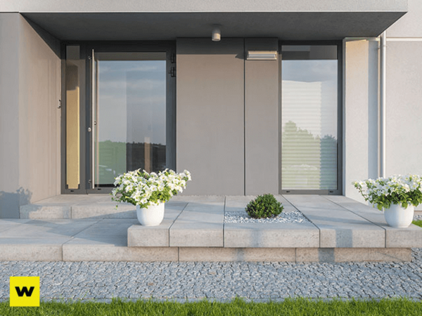 Moderner Hauseingang mit großen Fenstern, Steinterrasse und dekorativen Blumenkübeln.